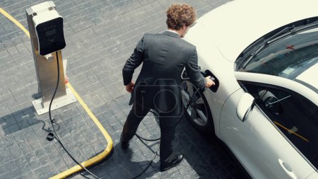 Photo for Progressive businessman install charger plug from charging station to his electric car before driving around city center. Eco friendly rechargeable car powered by sustainable and clean energy. - Royalty Free Image