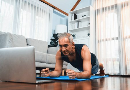 Photo for Athletic and sporty senior man planking on fitness exercising mat while watching online fitness video at home exercise as concept of healthy fit body lifestyle after retirement. Clout - Royalty Free Image