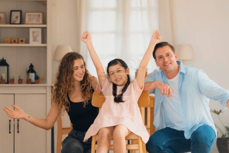 Photo for Happy family portrait with lovely little girl smiling and looking at camera, lovely and cheerful parent and their daughter sitting together in living room at home with warm daylight. Synchronos - Royalty Free Image
