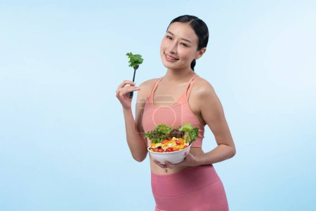 Photo for Young sporty Asian woman in sportswear holding salad bowl fill with vibrant of fruit and vegetable. Natural youthful and fit body lifestyle with balance nutrition on isolated background. Vigorous - Royalty Free Image