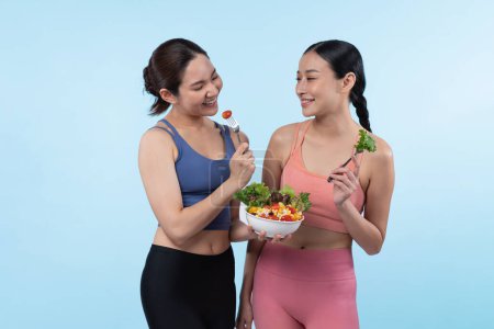 Téléchargez les photos : Deux jeunes femmes asiatiques sportives en tenue de sport tenant saladier remplissent de fruits et légumes. Naturel jeune et en forme mode de vie des gens avec équilibre nutritionnel sur fond isolé. Vigoureux - en image libre de droit