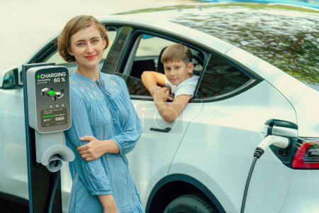 Téléchargez les photos : Famille de sensibilisation à l'environnement avec batterie de recharge de voiture électrique écologique à partir de la station de charge EV à la maison avec petit garçon à l'intérieur de la voiture. Technologie de voiture rechargeable et EV. Perpétuel - en image libre de droit