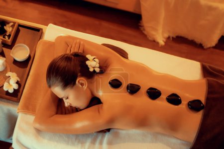 Photo for Panorama top view hot stone massage at spa salon in luxury resort with warm candle light, blissful woman customer enjoying spa basalt stone massage glide over body with soothing warmth. Quiescent - Royalty Free Image