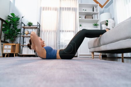 Photo for Young attractive asian woman in sportswear lies on the floor and doing sit-ups on the crouch, aiding targeting on abs muscle for effective home exercise routine. Vigorous - Royalty Free Image