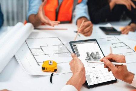 Photo for Diverse group of civil engineer and client working together on architectural project, reviewing construction plan and building blueprint using tablet at meeting table. Prudent - Royalty Free Image