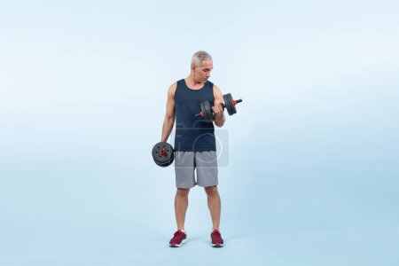 Photo for Full body length shot active and sporty senior man lifting dumbbell during weight training workout on isolated background. Healthy active physique and body care lifestyle for pensioner. Clout - Royalty Free Image