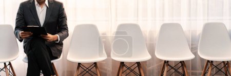 Photo for Job applicant waiting for interview in waiting room alone with empty chair on the corridor while applying on job application form. Modern employment and career seeker opportunity concept. Trailblazing - Royalty Free Image