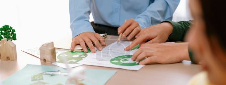 Photo for A cropped picture of green city poster was placed at green business meeting on meeting table with environmental document, wooden house block and windmill model scattered around. Closeup. Delineation. - Royalty Free Image