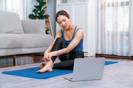 Foto de Mujer asiática en ropa deportiva sentada en el piso de la casa mientras ve videos de ejercicios en línea en el portátil. Chica atractiva participar en su búsqueda de un estilo de vida saludable. Vigoroso - Imagen libre de derechos