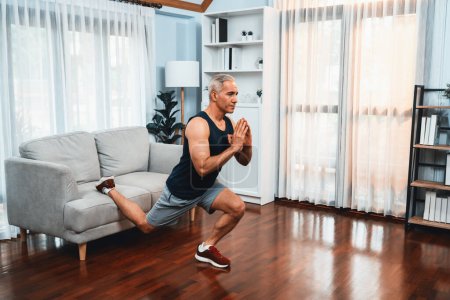 Photo for Active and fit senior man warmup and stretching using furniture before home exercising routine at living room. Healthy fitness lifestyle concept after retirement for pensioner. Clout - Royalty Free Image