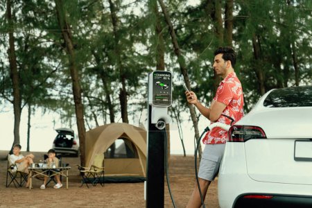 Photo for Outdoor adventure and family vacation camping in nature travel by eco friendly car for sustainable future. Lovely sit on trunk, charging EV car with EV charging station in campsite. Perpetual - Royalty Free Image