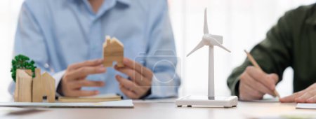 Photo for Business people invest in green business plan at meeting room on table with house model and wind mill placed represented eco house and renewable energy. Closeup. Delineation. - Royalty Free Image