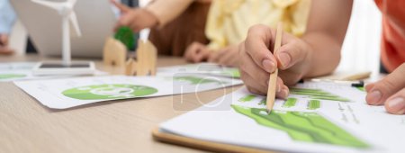 Photo for Windmill model represented using renewable energy placed during presenting green business on table with wooden block and environmental document scatter around. Closeup. Delineation. - Royalty Free Image