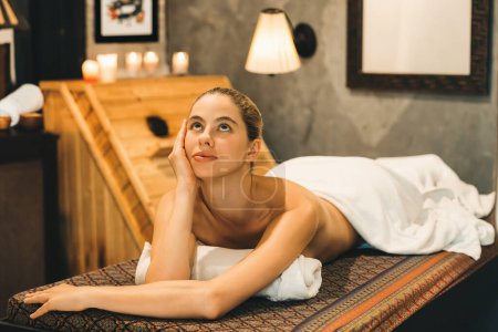 Téléchargez les photos : Portrait de belle femme caucasienne en serviette blanche femme se trouve sur un lit de spa en face de l'armoire de sauna en bois chaud avec détente et tranquillité au salon de spa. Ferme là. Une vue latérale. Tranquillité. - en image libre de droit