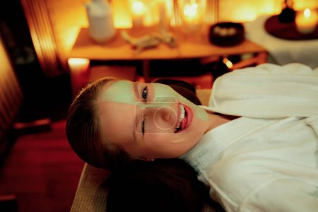 Téléchargez les photos : Ambiance sereine de salon de spa, femme cliente souriante et rajeunissante avec luxueux massage crème visage avec bougie lumineuse chaude. Soin du visage et concept de soins de beauté. Tranquillité - en image libre de droit