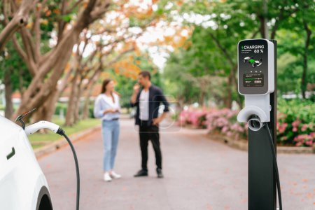 Photo for Focused EV car recharging battery on blurred background of lovey couple during autumnal road trip travel with electric vehicle recharging battery. Eco friendly travel on vacation during autumn. Exalt - Royalty Free Image