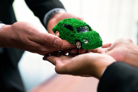 Téléchargez les photos : Les hommes d'affaires échangent et tiennent éco modèle de voiture verte. Véhicule électrique utilisé par la société écologique pour le transport respectueux de l'environnement. Entreprise zéro émission de CO2 responsable. Charmante. - en image libre de droit