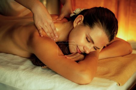 Téléchargez les photos : Femme caucasienne client appréciant relaxant massage spa anti-stress et dorloter avec beauté loisirs de la peau dans la bougie chaude éclairage spa salon d'ambiance à la station de luxe ou hôtel. Tranquillité - en image libre de droit