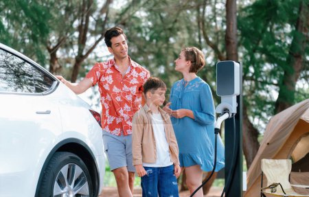 Photo for Outdoor adventure and family vacation camping in nature travel by eco friendly car for sustainable future. Lovely family recharge EV car with EV charging station in campsite. Perpetual - Royalty Free Image