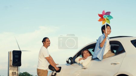 Photo for Concept of progressive happy family enjoying their time at wind farm with electric vehicle. Electric vehicle driven by clean renewable energy from wind turbine generator for charging station. - Royalty Free Image