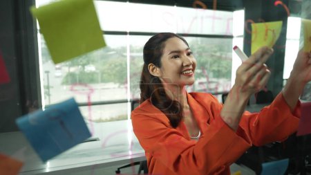 Photo for Professional young beautiful businesswoman thinking while standing at glass board with colorful sticky notes with marketing idea written. Portrait of project manager looking at mind map. Manipulator. - Royalty Free Image