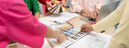 Photo for Professional designer team brainstorms material colors, while the project manager suggests a suitable color at meeting table with architectural equipment and color palette scatter around. Variegated. - Royalty Free Image