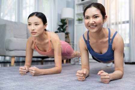 Photo for Fit young asian woman planing on the living room floor with her trainer or exercise buddy. Healthy lifestyle workout training routine at home. Balance and endurance exercising concept. Vigorous - Royalty Free Image