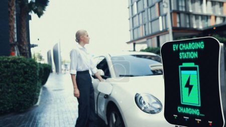Photo for Businesswoman recharge her electric car from charging station at city center or public parking car. Eco friendly rechargeable car using alternative clean energy. Peruse - Royalty Free Image