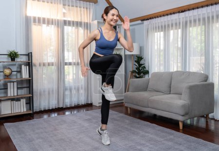 Foto de Enérgica y fuerte atlética mujer asiática corriendo en su lugar en su casa. Búsqueda de físico en forma y compromiso con un estilo de vida saludable con entrenamiento en casa y entrenamiento. Vigoroso - Imagen libre de derechos