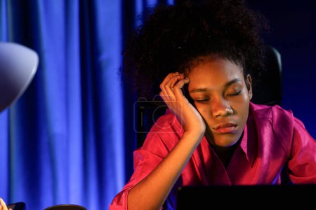 Photo for Exhausted and sleepy young African businesswoman taking a nap in her arm on desk at home office. Concept of thinking a lot projects until sleeping among unfinished online work. Tastemaker. - Royalty Free Image
