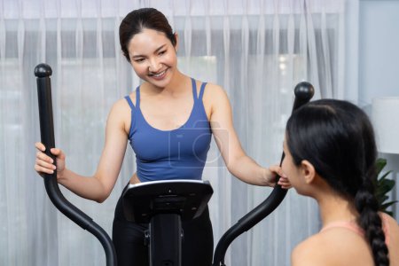 Photo for Energetic and strong athletic asian woman running on elliptical running machine at home with workout buddy or trainer. Pursuit of fit physique and commitment to healthy lifestyle. Vigorous - Royalty Free Image