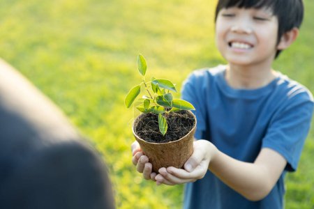 Téléchargez les photos : Promouvoir la sensibilisation à l'éco-reboisement et la durabilité environnementale à long terme avec le garçon asiatique tenant la plante. Favoriser une nature plus verte pour les générations futures grâce à un écosystème durable. Pneumatique - en image libre de droit