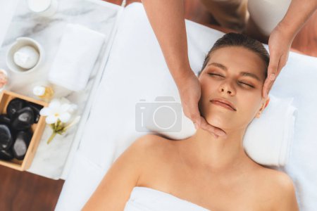 Téléchargez les photos : Panorama vue de dessus de la femme appréciant relaxant anti-stress massage de la tête et dorloter beauté faciale loisirs de la peau dans dayspa moderne lumière ambiante au complexe de luxe ou un salon de spa de l'hôtel. Tranquillité - en image libre de droit