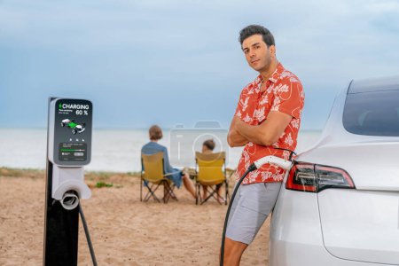 Photo for Family vacation trip traveling by the beach with electric car, dad or father recharge EV car while his family enjoy seascape beach. Family trip with alternative energy and eco-friendly car. Perpetual - Royalty Free Image
