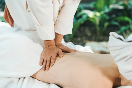 Photo for A pretty girl with beautiful skin with white towel receives back massage from Thai professional masseur surrounded by relaxing and peaceful spa environment. Closeup. Focus on back.Tranquility. - Royalty Free Image