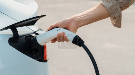 Téléchargez les photos : Closeup main mis chargeur EV pour recharger la batterie des voitures électriques de la station de charge dans le stationnement commercial de la ville. Voiture rechargeable pour des déplacements urbains respectueux de l'environnement. Expedient - en image libre de droit