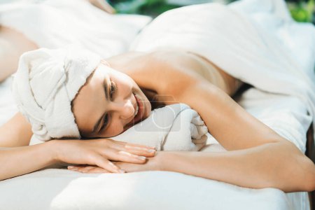 Téléchargez les photos : Un portrait d'une jolie fille de spa en serviette blanche se trouve sur un lit de spa en attendant un massage en plein air entouré d'un environnement naturel relaxant avec son ami. Fond flou. Tranquillité. - en image libre de droit