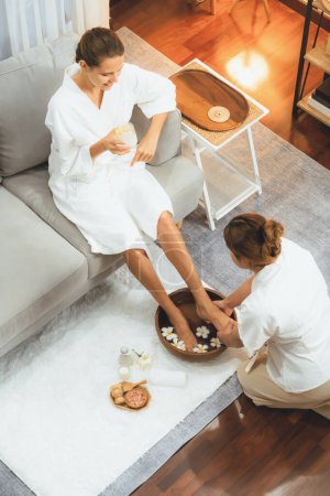 Téléchargez les photos : Femme se livre à un massage des pieds heureux au salon de spa de luxe tandis que masseur donner thérapie de réflexologie dans une douce ambiance de lumière du jour station ou spa des pieds de l'hôtel. Tranquillité - en image libre de droit