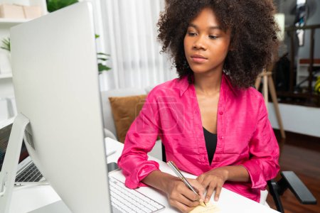 Téléchargez les photos : Femme d'affaires afro-américaine créer des emplois de projet client sur ordinateur avec debout sur le bureau au bureau à domicile, écrire des informations cruciales sur le papier. Concept de vie professionnelle créative. Tastemaker. - en image libre de droit