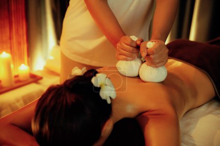 Photo for Hot herbal ball spa massage body treatment, masseur gently compresses herb bag on woman body. Tranquil and serenity of aromatherapy recreation in warm lighting of candles at spa salon. Quiescent - Royalty Free Image