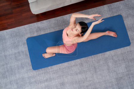 Photo for Top view asian woman in sportswear doing yoga exercise on fitness mat as her home workout training routine. Healthy body care and calm meditation in yoga lifestyle. Vigorous - Royalty Free Image