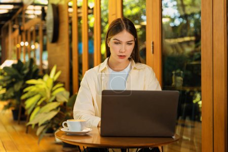 Photo for Young woman working on laptop at outdoor cafe garden during springtime, enjoying serenity ambient at coffee shop. Digital nomad freelancer or college student working remotely or blogging. Expedient - Royalty Free Image