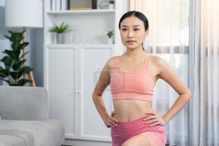 Téléchargez les photos : Jeune femme asiatique attrayante en vêtements de sport étirement avant la routine d'exercice de remise en forme. Entraînement du corps à domicile avec une femme athlétique saine échauffement. Vigoureux - en image libre de droit