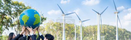 Foto de Concepto del Día de la Tierra con gran globo terráqueo sostenido por el equipo de empresarios asiáticos promoviendo la conciencia ambiental utilizando energía limpia sostenible y renovable con turbina eólica para un futuro más verde. Gyre. - Imagen libre de derechos