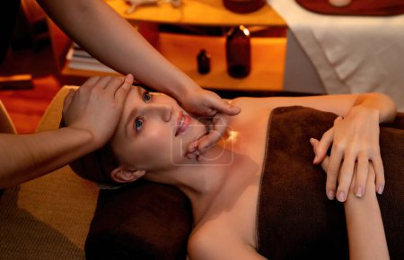 Téléchargez les photos : Femme caucasienne profiter relaxant anti-stress massage de la tête et choyer beauté faciale loisirs de la peau dans la bougie chaude éclairage spa salon ambiant dans un complexe de luxe ou un hôtel. Tranquillité - en image libre de droit