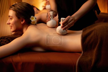 Heiße Kräuterball-Wellness-Massage Körperbehandlung, Masseur sanft komprimiert Kräuterbeutel auf Paar Kunden Körper. Gelassenheit der Aromatherapie Erholung im warmen Entzünden von Kerzen im Kursalon. Ruhige Lage