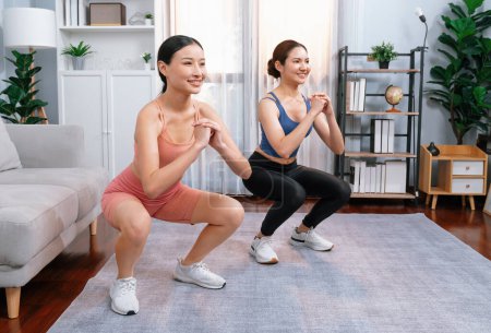 Photo for Vigorous energetic woman with trainer or workout buddy doing exercise at home. Young athletic asian woman strength and endurance training session as home workout routine with squat. - Royalty Free Image