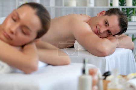 Téléchargez les photos : Blissful couple client ayant un traitement d'exfoliation dans le salon de spa de luxe avec lumière de bougie de chaleur ambiante. Sel gommage soin de beauté dans le gommage du corps spa de santé. Tranquillité - en image libre de droit