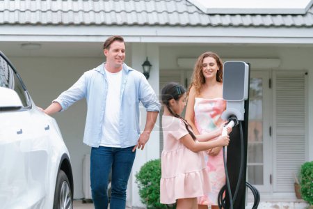 Photo for Happy little young girl learn about eco-friendly and energy sustainability as she help her family recharge electric vehicle from home EV charging station. EV car and modern family concept. Synchronos - Royalty Free Image