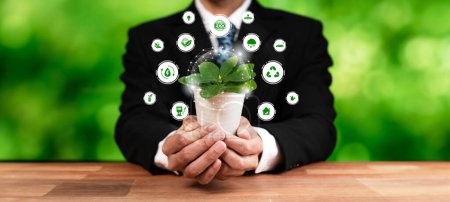 Téléchargez les photos : Un homme d'affaires tenant une usine verte avec une icône de design numérique écologique symbolise une entreprise respectueuse de l'environnement avec l'engagement ESG de réduire les émissions de carbone en utilisant une énergie propre et durable. Dépendance - en image libre de droit